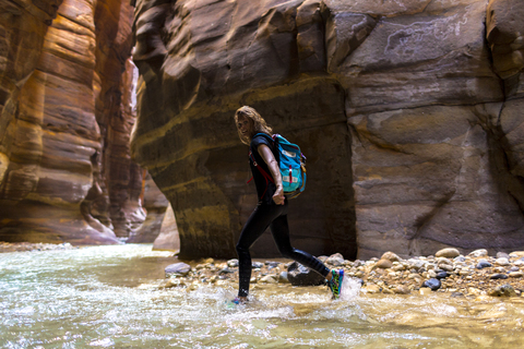 Portrait of female backpacker walking in river by mountains stock photo