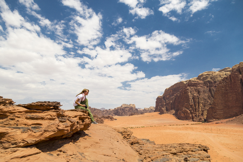 Woman sitting on rock against sky on sunny day stock photo