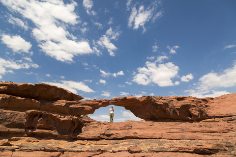 Woman looking up while standing on rock formation against sky stock photo