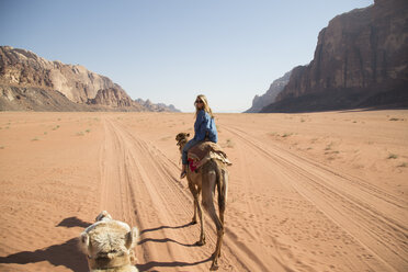 Weibliche Touristin schaut beim Reiten auf einem Kamel in der Wüste über die Schulter - CAVF28395