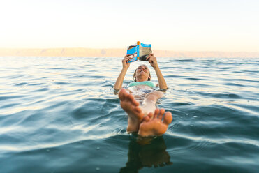 Frau liest ein Buch, während sie im Meer schwimmt - CAVF28401