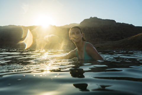 Woman swimming in sea against mountain during sunset stock photo
