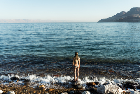 Rear view of woman looking at sea while standing on rock stock photo