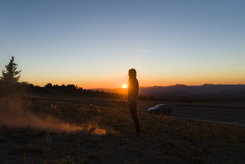 Seitenansicht einer auf einem Feld stehenden Frau gegen den Himmel bei Sonnenuntergang, lizenzfreies Stockfoto
