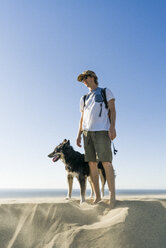 Mann mit Hund am Strand stehend gegen klaren blauen Himmel - CAVF28432