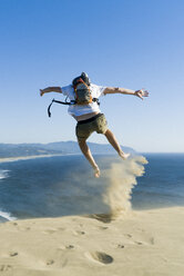 Rear view of playful man jumping on sand at beach against clear blue sky - CAVF28433