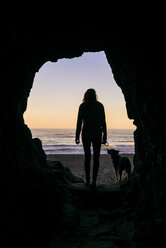 Silhouette Frau mit Hund stehend am Höhleneingang gegen Strand - CAVF28442