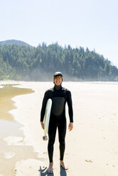 Porträt eines glücklichen Mannes, der ein Surfbrett hält, während er am Strand steht - CAVF28451