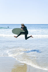 Mann mit Surfbrett springt ins Meer gegen klaren Himmel - CAVF28455