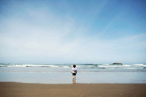 Rückansicht eines am Strand stehenden Mädchens gegen den Himmel an einem sonnigen Tag, lizenzfreies Stockfoto