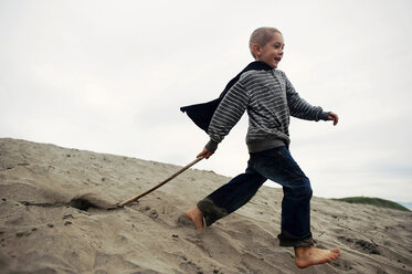 Verspielter Junge mit Stock auf Sand am Strand gegen den Himmel - CAVF28497