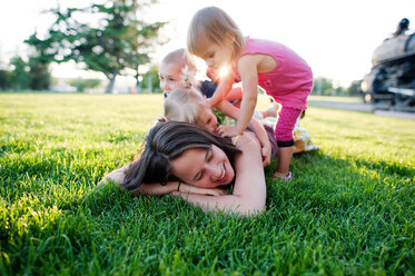 Children playing with mother lying on grassy field at park - CAVF28507