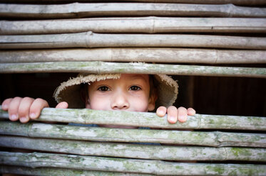 Porträt eines Jungen, der durch einen Bambuszaun schaut - CAVF28515