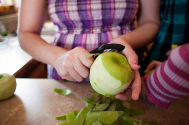 Mittelteil einer Frau, die einen Apfel am Küchentisch schält - CAVF28517