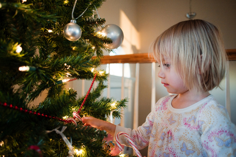 Mädchen berührt Weihnachtsbaum zu Hause, lizenzfreies Stockfoto