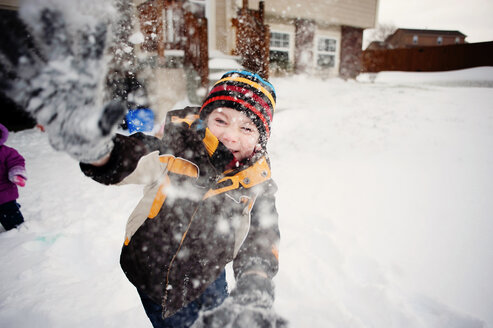 Porträt eines glücklichen Jungen, der mit Schnee im Garten spielt - CAVF28524