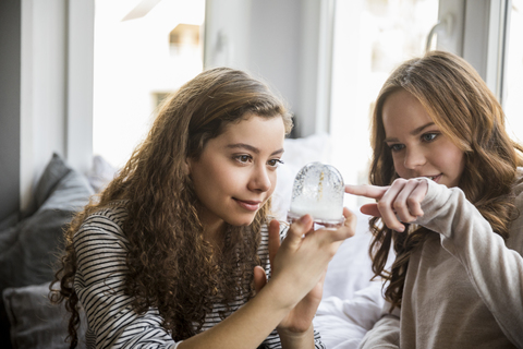 Zwei Mädchen im Teenageralter mit Schneekugel zu Hause, lizenzfreies Stockfoto