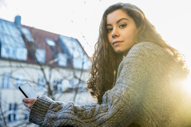 Portrait of teenage girl with smartphone at backlight - FMKF05004