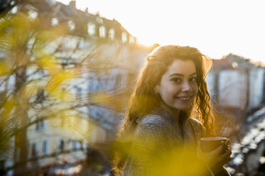 Portrait of laughing teenage girl with coffee mug on balcony at twilight - FMKF05009