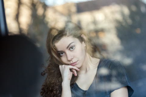 Porträt eines nachdenklichen Teenagers hinter einer Fensterscheibe, lizenzfreies Stockfoto