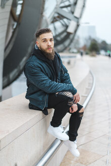 Frankreich, Paris, Porträt eines bärtigen jungen Mannes, der an einer Wand sitzt - AFVF00365