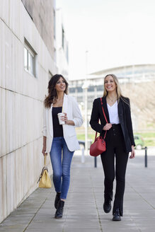 Zwei entspannte Geschäftsfrauen mit Handtaschen und Kaffee zum Spazierengehen auf dem Bürgersteig - JSMF00138