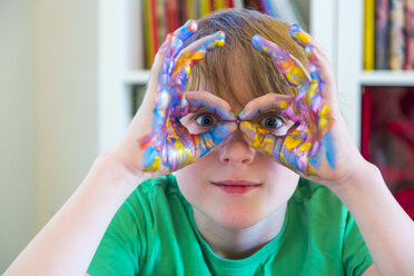 Boy looking through fingers, hands with finger paints - SARF03623