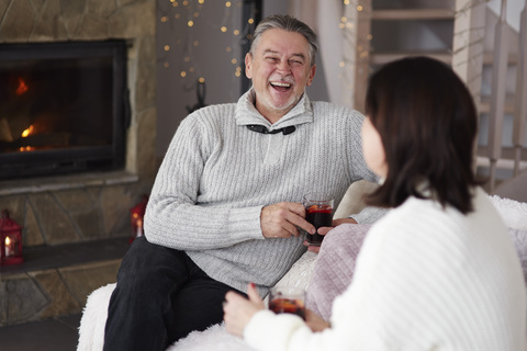 Glückliches reifes Paar mit heißen Getränken im Wohnzimmer, lizenzfreies Stockfoto