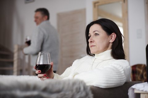 Ernste reife Frau mit einem Glas Wein und einem Mann im Hintergrund, lizenzfreies Stockfoto