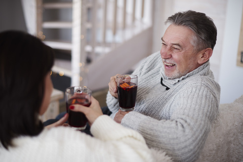 Happy mature couple with hot drinks in living room stock photo