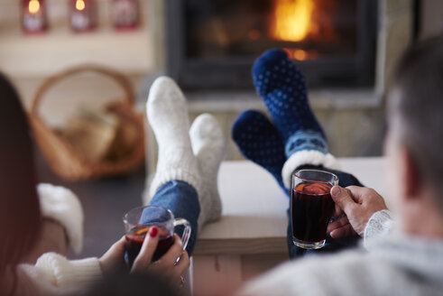 Mature couple with hot drinks in living room at the fireplace - ABIF00195