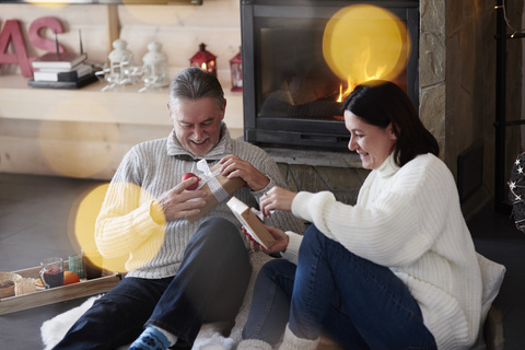 Happy mature couple at the fireplace unpacking gifts stock photo