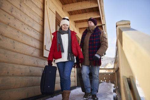 Älteres Paar mit Koffern beim Wandern auf einer Berghütte im Winter - ABIF00201