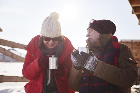 Happy mature couple with hot drinks outdoors at mountain hut in winter stock photo