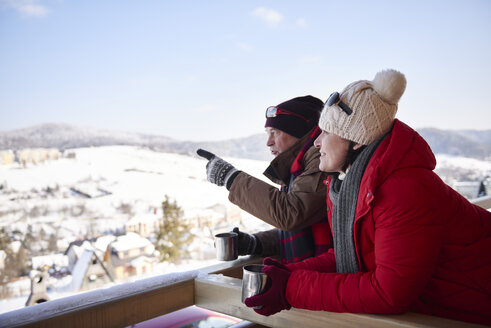 Älteres Paar mit heißen Getränken im Gespräch im Freien mit Blick auf die Winterlandschaft - ABIF00206