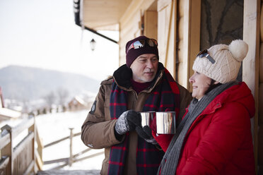 Älteres Paar mit heißen Getränken im Gespräch im Freien auf einer Berghütte im Winter - ABIF00207