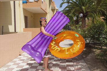 Lächelnde Frau steht vor einem Hotel und hält ein aufblasbares Floß und einen Ring - FOLF00167