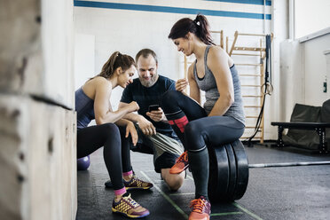 Junge Frauen und Mann schauen im Fitnessstudio auf das Telefon - FOLF00412