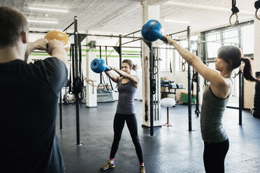 Junge Frauen und Mann schwingen Kettlebells im Fitnessstudio - FOLF00424