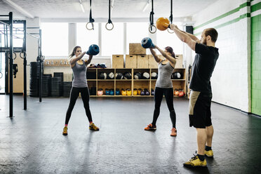 Junge Frauen und Mann schwingen Kettlebells im Fitnessstudio - FOLF00426