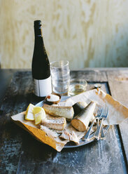 Smoked fish, lemon, cutlery and bottle of wine on wooden table - FOLF00517