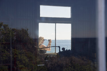 Frau durch Fenster gesehen, die das Meer fotografiert - FOLF00613