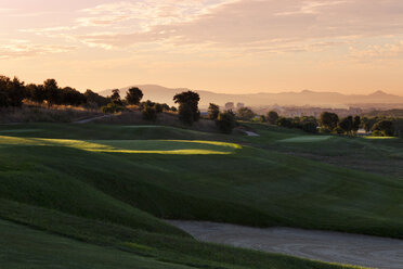 Grasbewachsene Hügel des Golfplatzes im Schatten mit entfernter Stadtlandschaft im Hintergrund - FOLF00618