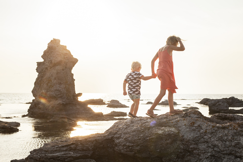 Mädchen geht mit Bruder auf Küstenfelsen spazieren, lizenzfreies Stockfoto