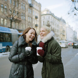 Zwei Frauen halten lachend Einweg-Kaffeebecher - FOLF00802