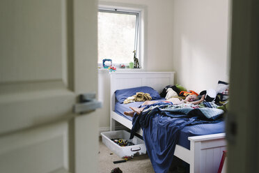 Boy sleeping on bed at home seen through doorway - CAVF28536