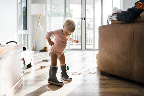 Kleinkind trägt Gummistiefel, während es zu Hause am Schnuller nuckelt - CAVF28537