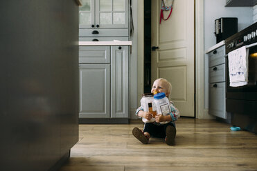 Kleinkind hält Plastikgläser, während es zu Hause in der Küche auf dem Boden sitzt - CAVF28545
