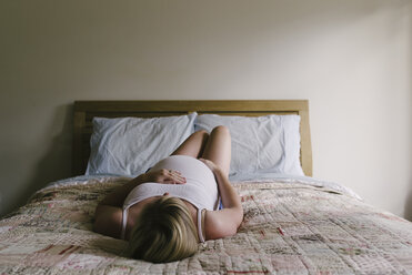 Schwangere Frau auf dem Bett liegend mit Händen auf dem Bauch gegen die Wand zu Hause - CAVF28548
