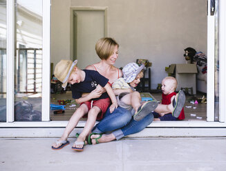 Mother playing with children while sitting on doorway at home - CAVF28549